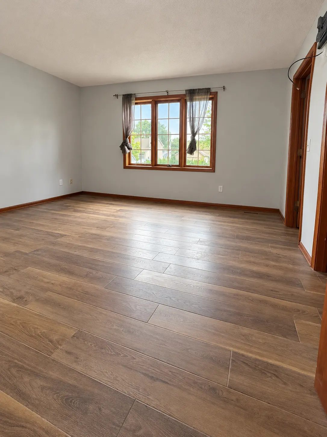 Room after the improvements, with finished flooring, painted walls, and a window with tied curtains
